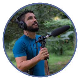 Luis Sandoval holding microphone in field to record bird songs