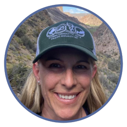 Anna Chalfoun wearing baseball cap with Wyoming Cooperative Fish & Wildlife Research Unit insignia while standing in mountain valley.